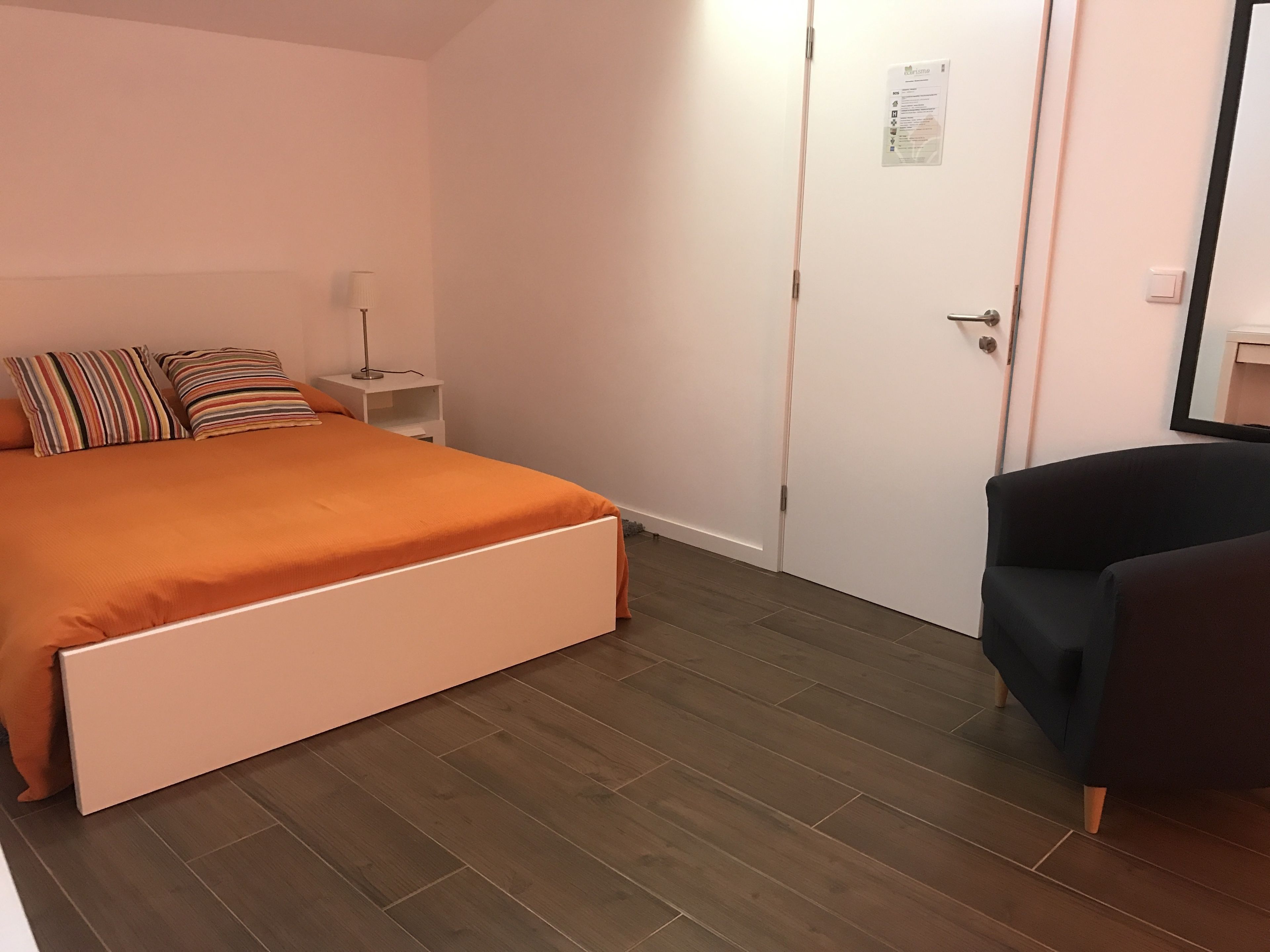 A bedroom with a bed, pillows, a nightstand, a chair, and a door.