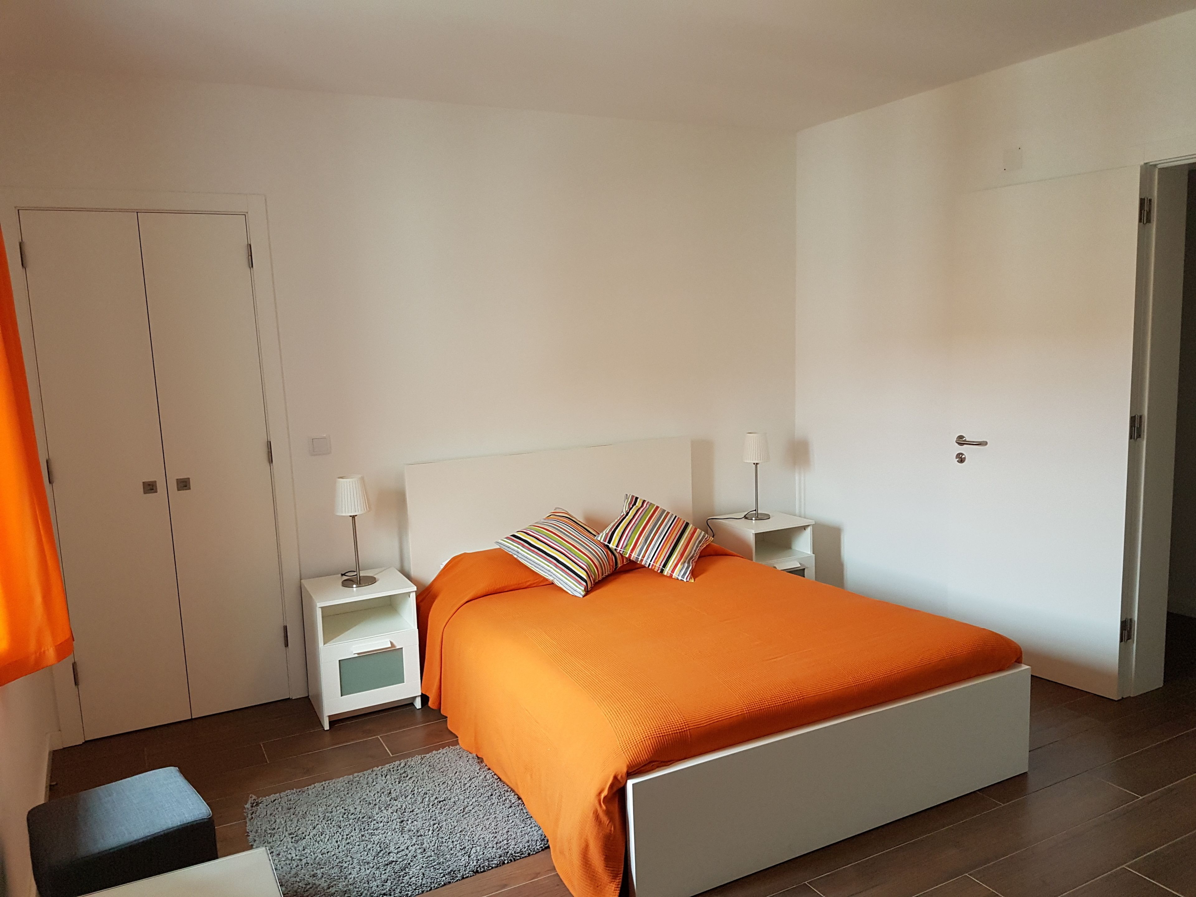 A bedroom with a bed, nightstands, a wardrobe, and a door.