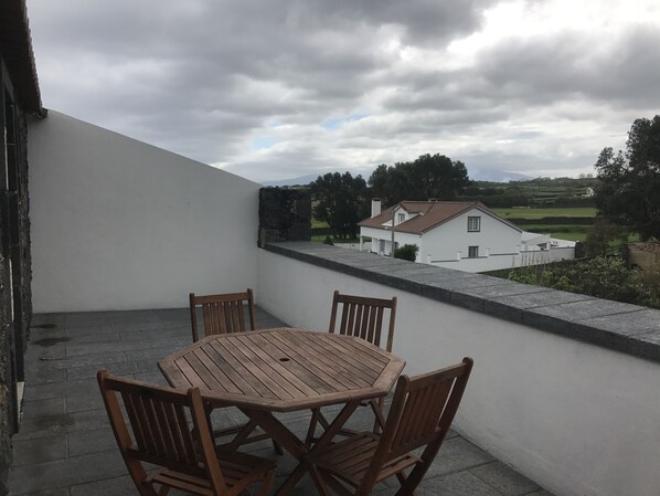 A wooden table and chairs on a balcony with a view of a white house and surrounding greenery. - Stonewood Lodge (Ponta Delgada)