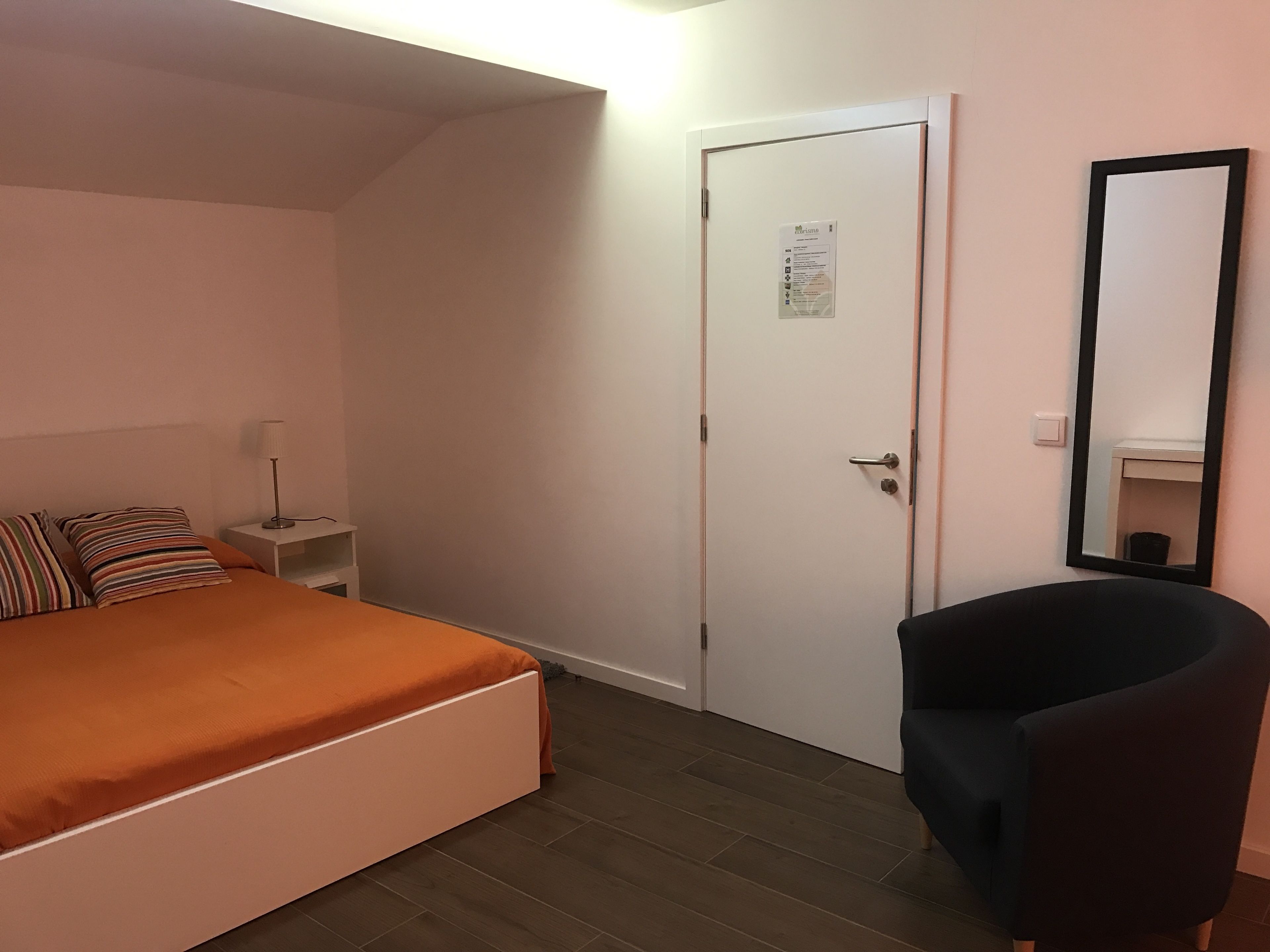 A bedroom with a bed, a nightstand, a chair, a door, and a mirror.