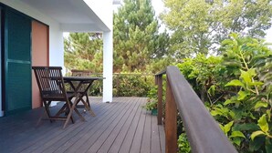 Eine Holzterrasse mit Tisch und Stühlen, umgeben von Grünpflanzen und Bäumen.