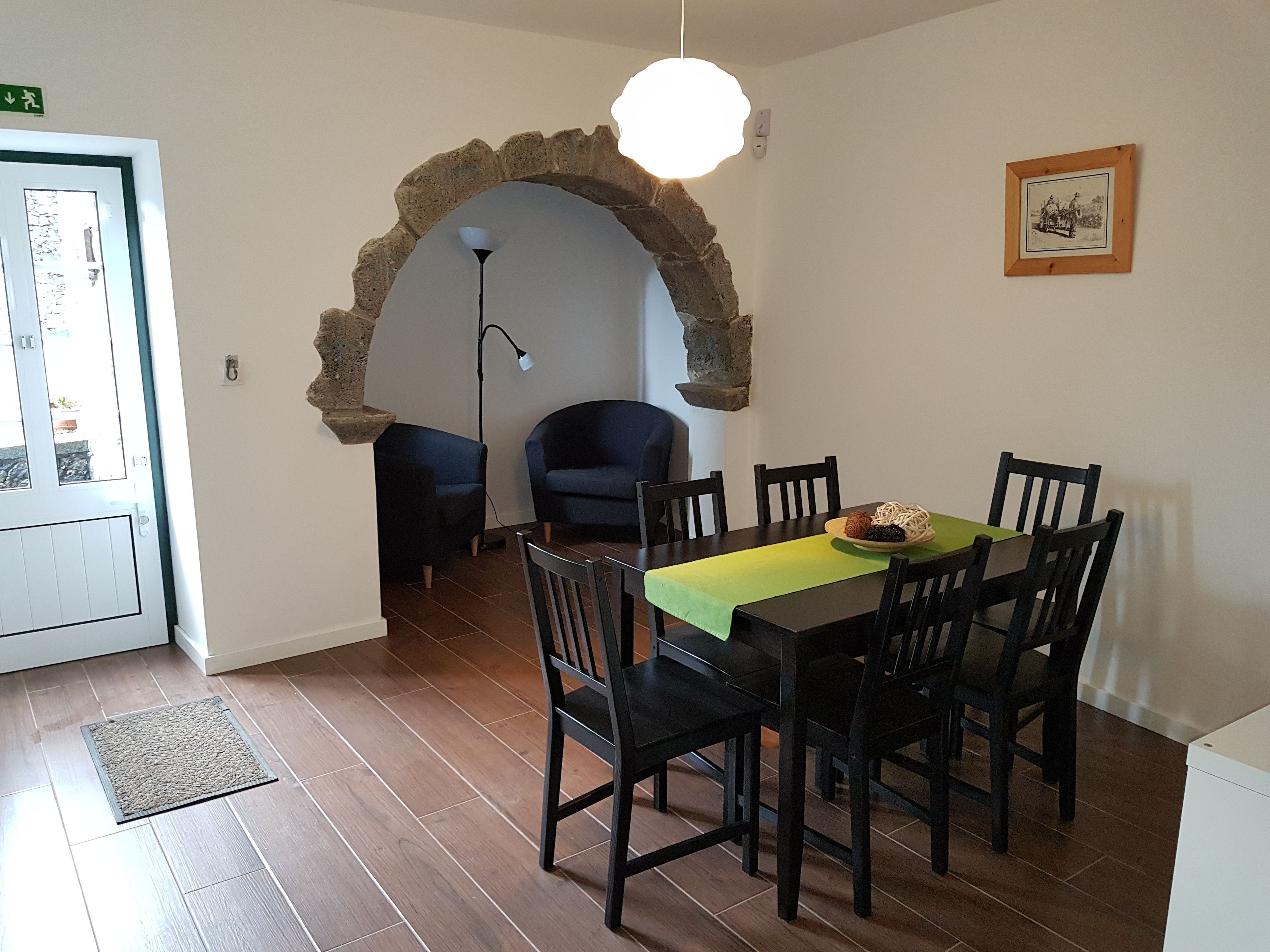 A dining area with a table set for four, surrounded by chairs, under a stone archway.