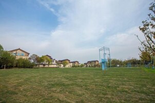 Un campo cubierto de césped con una estructura azul, posiblemente una instalación deportiva, y casas al fondo.