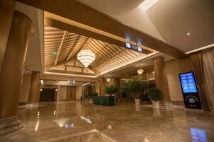 Un vestíbulo de hotel con piso de mármol pulido, una mesa de recepción, una araña y un panel informativo digital.
