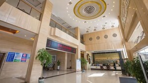Eine geräumige Lobby mit hoher Decke, einem Empfangstresen und einer großen digitalen Anzeige.