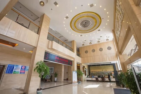 A spacious lobby with a high ceiling, a reception desk, and a large digital sign.
