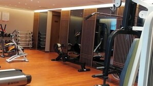 Ein Fitnessraum mit Trainingsgeräten, Holzboden und einer Spiegelwand.