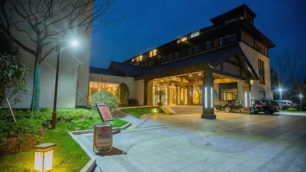 A hotel entrance at night with a well-lit driveway, a signboard, and a car parked outside.