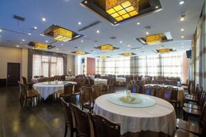 A banquet hall with round tables, chairs, and ceiling lights.
