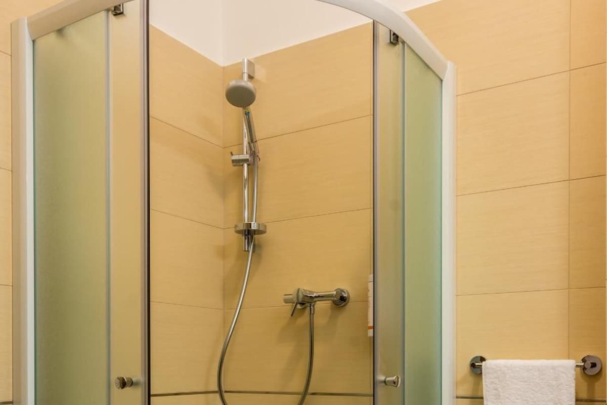 A glass-enclosed shower stall with a handheld showerhead and a towel rack with a white towel.