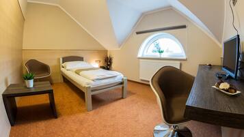 A compact hotel room with a bed, a desk, a chair, a small table, and a window.