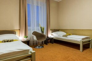 A hotel room with two single beds, a chair, a nightstand, and a window with curtains.