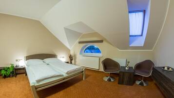 A bedroom with a bed, two chairs, a small table, a radiator, and a window with a view.