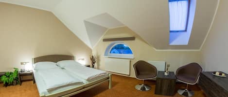 Un dormitorio con cama, dos sillas, una mesita, un radiador y ventana con vistas.