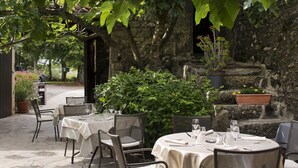 An outdoor dining area with stone walls, potted plants, and tables set for dining. - Logis Auberge les Murets (Chandolas)