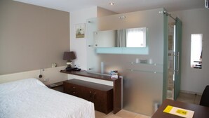 A hotel room with a bed, a desk with a lamp, a mirror, and a shower area. - Logis Auberge les Murets (Chandolas)