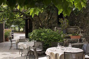 An outdoor dining area with stone walls, potted plants, and tables set for dining. - Logis Auberge les Murets (Chandolas)