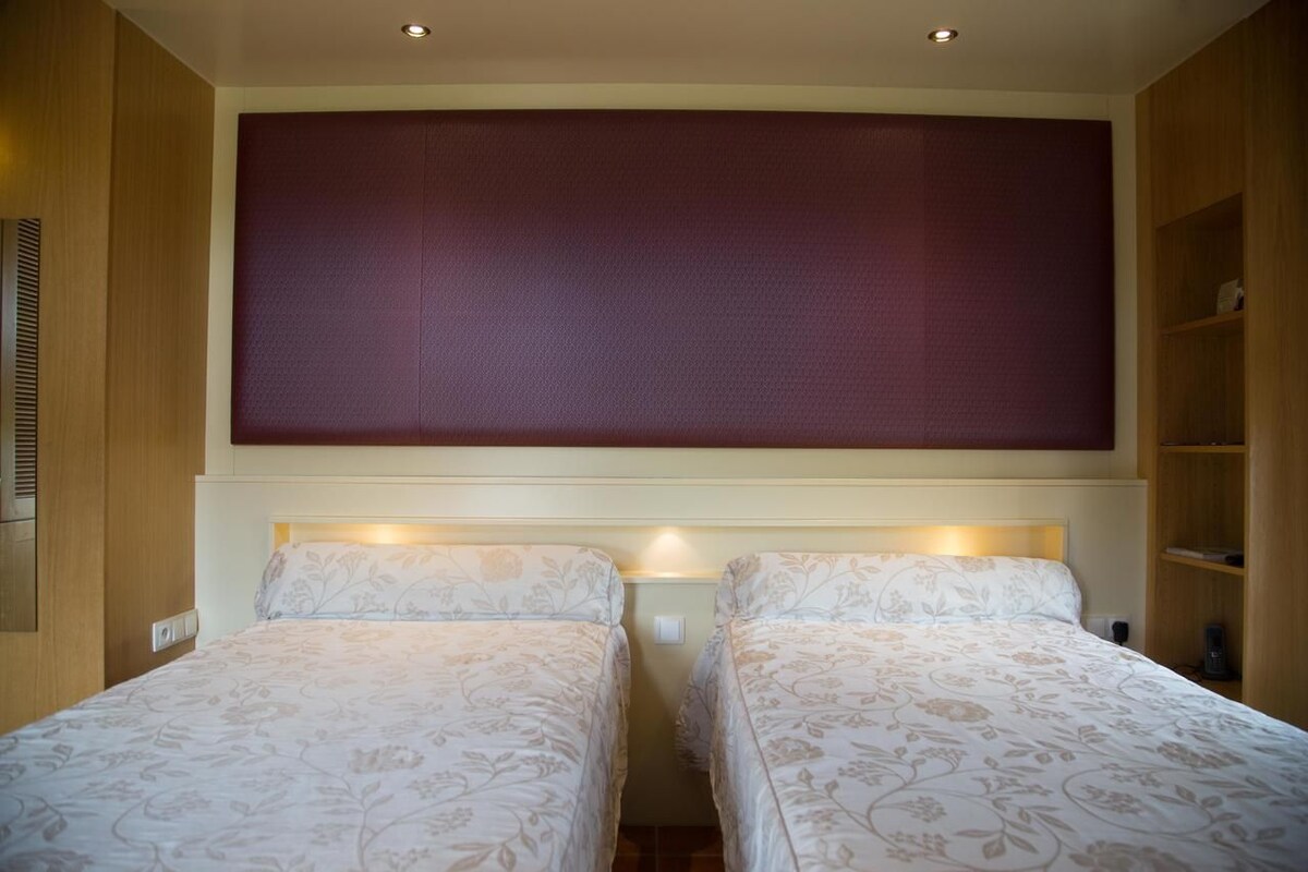 Habitación de hotel con dos camas, un cabecero grande y acolchado, y estantes empotrados.
