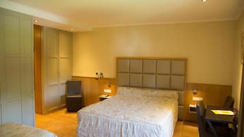 Habitación de hotel con una cama grande, un escritorio y una silla. Hay dos mesitas de noche con lámparas. La habitación tiene un cabecero de madera y un armario.