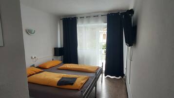 Quarto com cama, mesa de cabeceira, janela com cortinas e vista para o exterior.