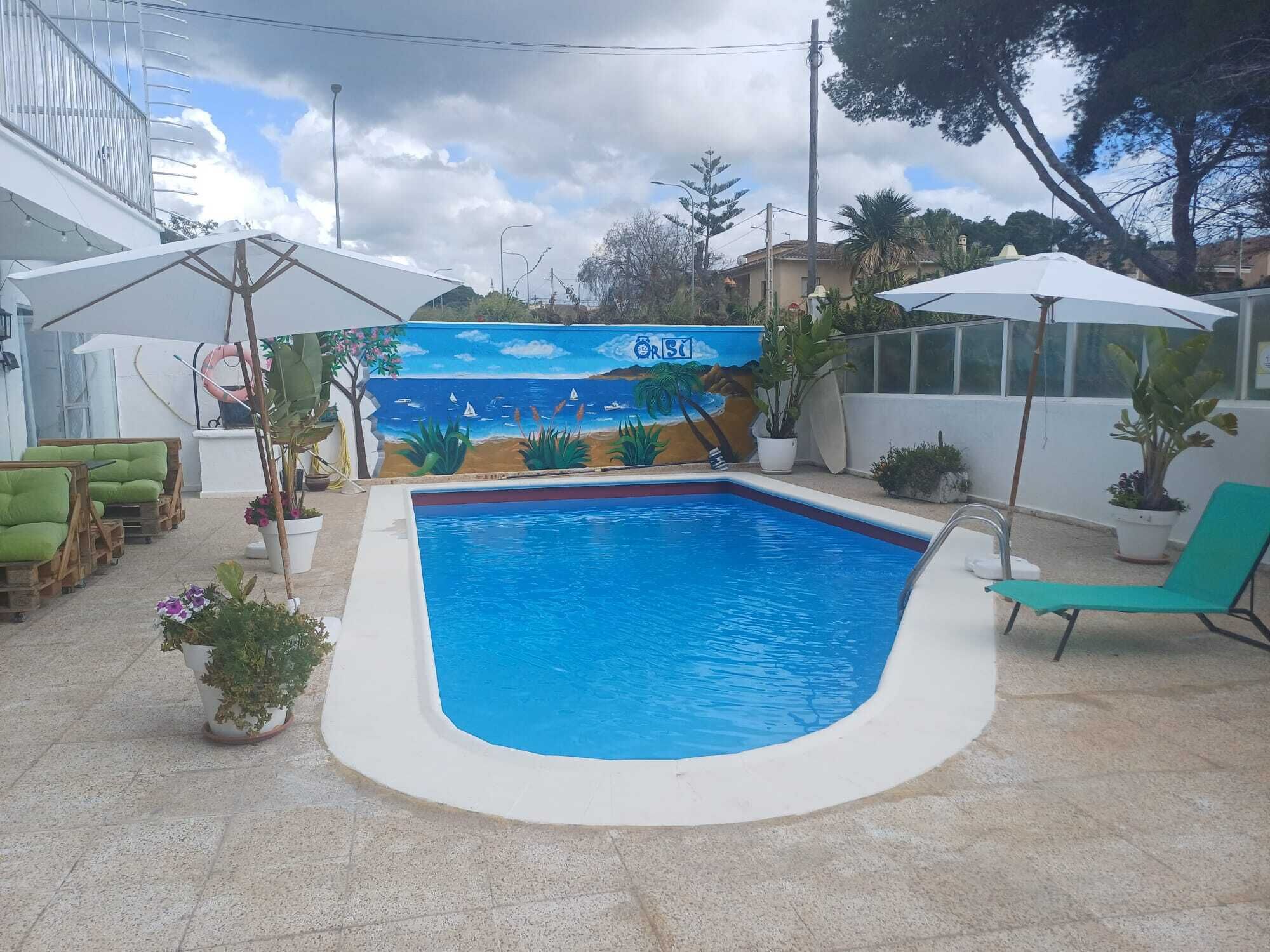Una piscina con un mural, mobiliario exterior y plantas en macetas.