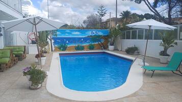 Una piscina con un mural, mobiliario exterior y plantas en macetas.