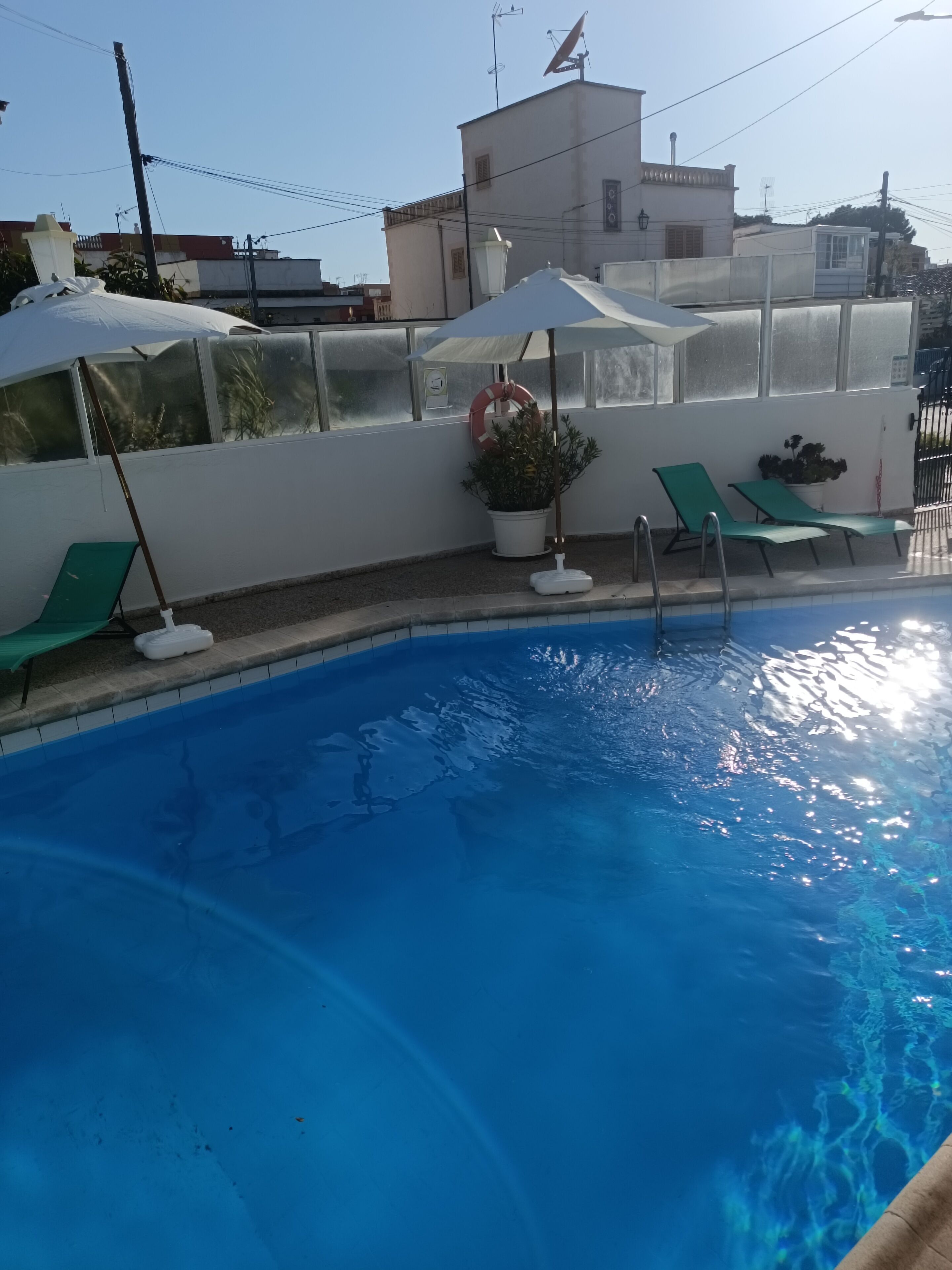 Una piscina con agua azul cristalina, rodeada de sillas de descanso y sombrillas verdes.
