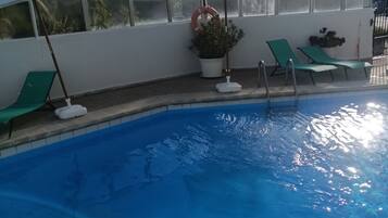 Una piscina con agua azul cristalina, rodeada de sillas de descanso y sombrillas verdes.