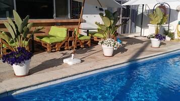 A poolside area with a clear blue pool, wooden lounge chairs, and potted plants.