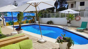 Piscina com mural, área de estar ao ar livre e guarda-sóis.