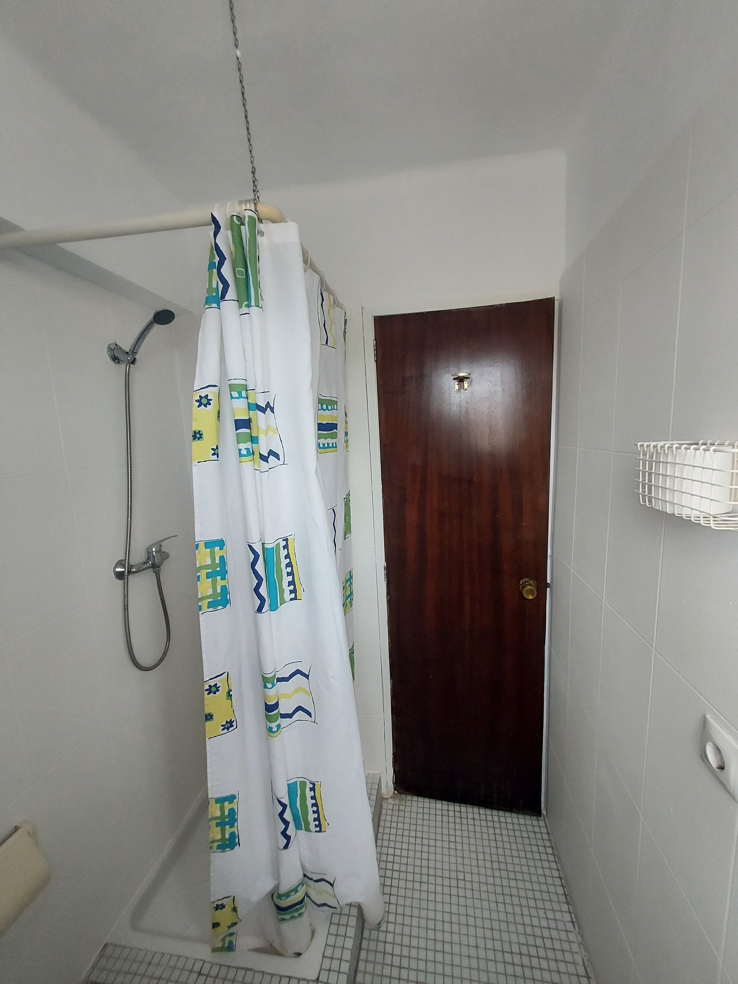 Een badkamer met douchegordijn, een houten deur en betegelde muren.