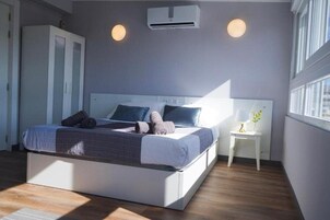 Un dormitorio moderno con cama, armario empotrado, mesita de noche y ventana que deja entrar luz natural.