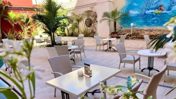 An outdoor patio with wicker furniture, a mural of a beach scene, and tropical plants. - Xapala (MALLORCA)