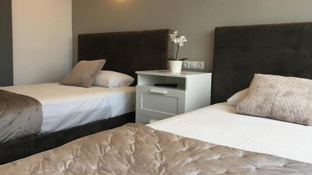 Ein Hotelzimmer mit zwei Einzelbetten, einem Nachttisch mit Lampe und einem kleinen Tisch mit Blumenvase.