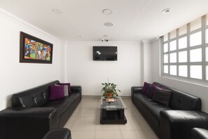 Een moderne woonkamer met twee zwarte leren banken, een glazen salontafel, een ingelijst abstract schilderij, een flatscreen televisie en een groot raam.