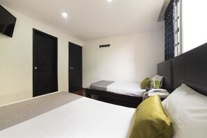 Een hotelkamer met een groot bed, een kleiner bed, een bureau met telefoon en een raam met gordijnen.