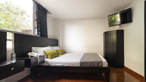 A modern hotel room with a bed, bedside table, TV, wardrobe, and a window with curtains. - Hotel Dorado 100 (Bogotá)