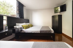 Une chambre d’hôtel moderne équipée d’un lit, d’une table de chevet, d’une télévision, d’une armoire et d’une fenêtre avec des rideaux.