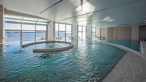 An indoor swimming pool with clear views of the sea through large windows, a circular hot tub, and a poolside area with chairs. - Hotel Vile Park Premium (Piran)