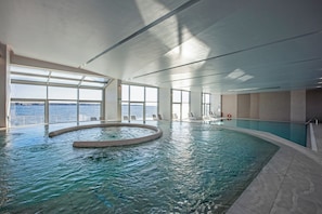An indoor swimming pool with clear views of the sea through large windows, a circular hot tub, and a poolside area with chairs. - Hotel Vile Park Premium (Piran)