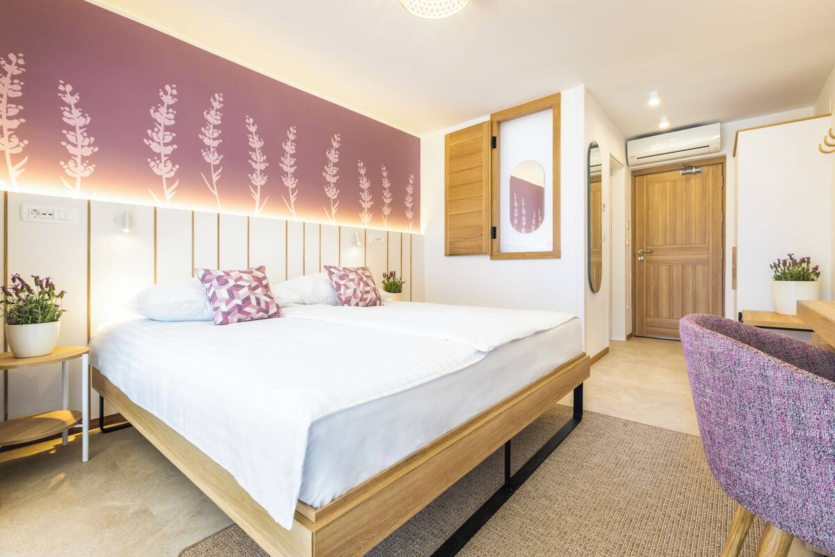 Un dormitorio moderno con una cama grande, mesitas de noche, una silla, un espejo fijado a la pared y una puerta.