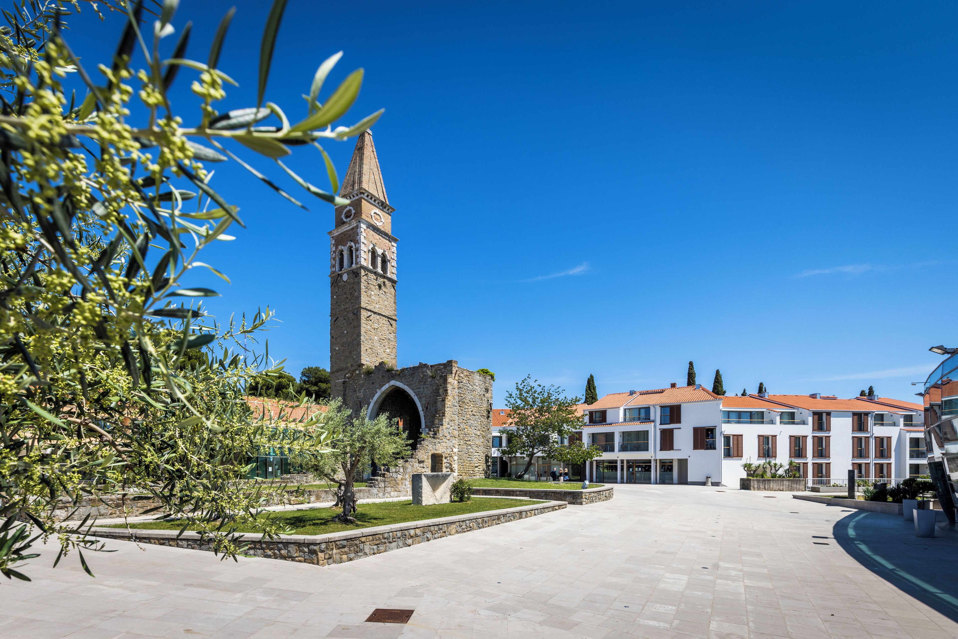 Un cortile con una torre storica, edifici moderni e un giardino curato.