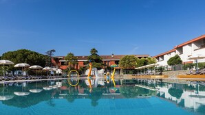 A swimming pool with lounge chairs and umbrellas, surrounded by buildings with a tiled roof. - Hotel Vile Park Premium (Piran)