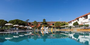 A swimming pool with lounge chairs and umbrellas, surrounded by buildings with a tiled roof. - Hotel Vile Park Premium (Piran)