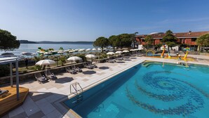 A pool area with sun loungers and umbrellas, a clear view of the sea, and a building with a tiled roof. - Hotel Vile Park Premium (Piran)