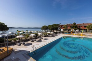 A pool area with sun loungers and umbrellas, a clear view of the sea, and a building with a tiled roof. - Hotel Vile Park Premium (Piran)