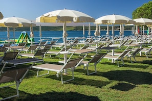 Rows of sun loungers and umbrellas on a grassy area by a body of water. - Hotel Vile Park Premium (Piran)