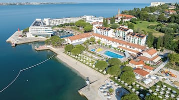 An aerial view of a coastal hotel with a swimming pool, multiple buildings, and a marina.