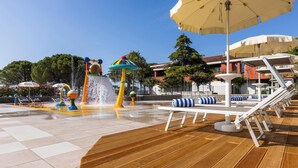 Un área de juegos acuáticos con estructuras coloridas, una terraza de madera y asientos exteriores con sombrillas.