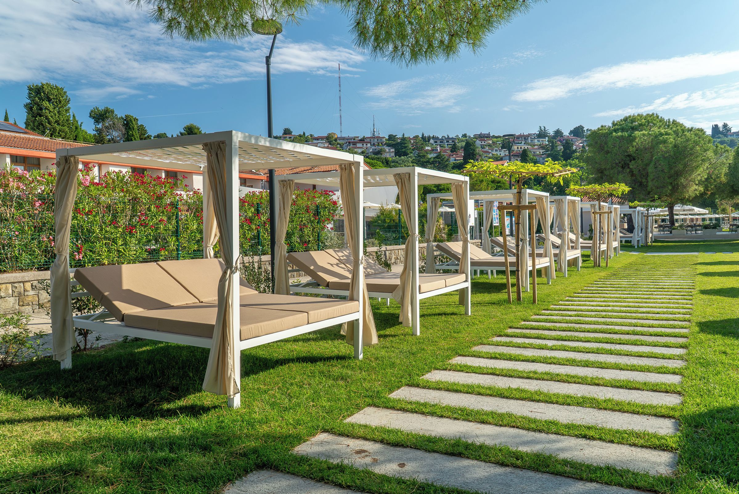 Zonas de estar al aire libre con toldos, un camino de piedra y vistas a una zona residencial al fondo.